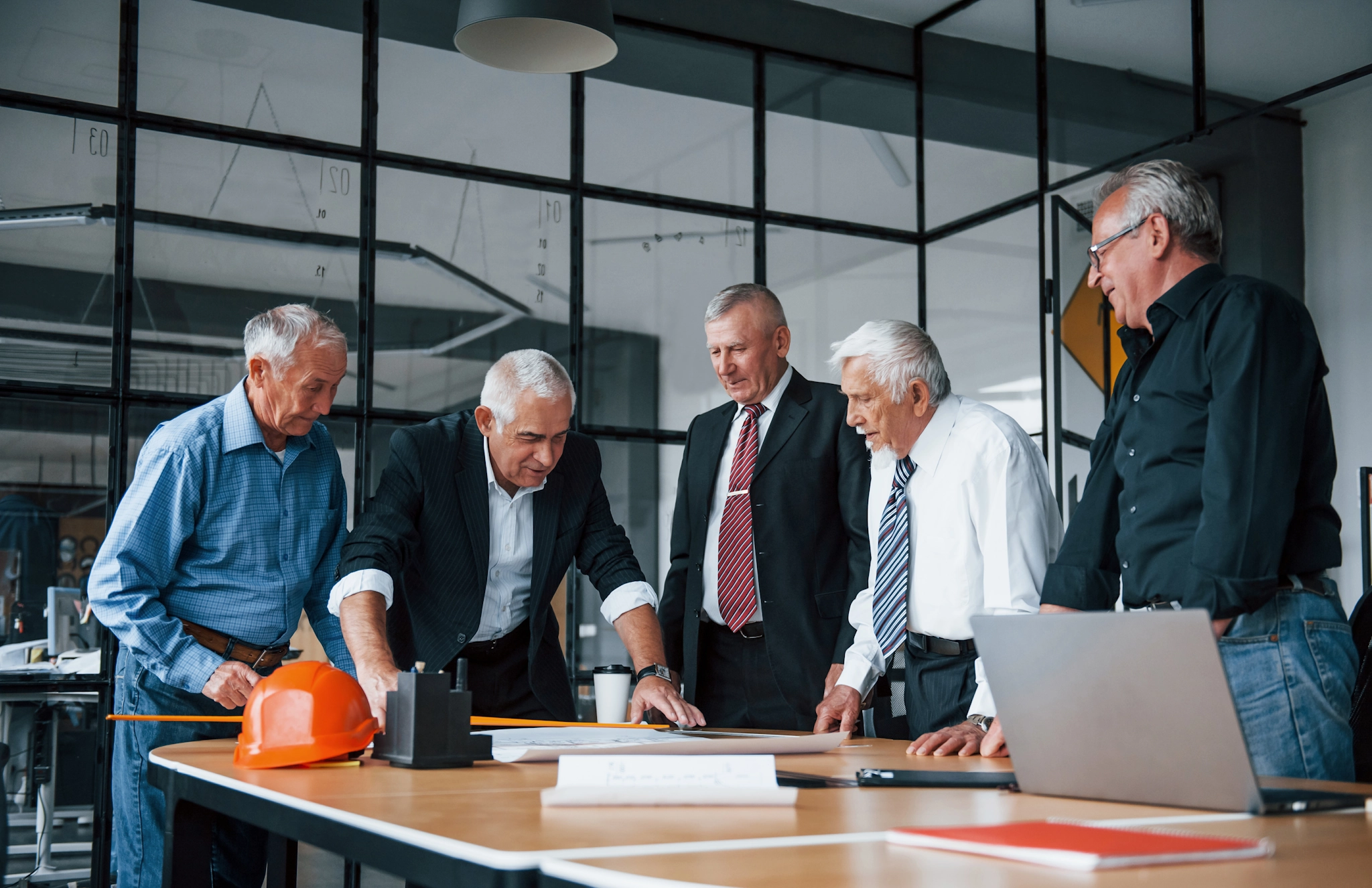 Une équipe d'architectes âgés travaille sur un plan au bureau – symbole de collaboration et de planification partagée.